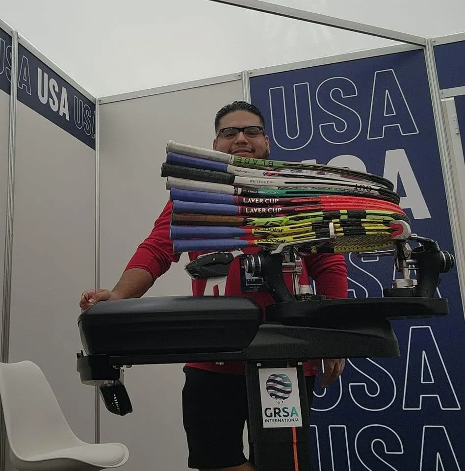 Dimas Méndez at his stringing machine with a stack of freshly strung tour racquets